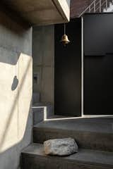 Visitors ascend a concrete staircase and pass through a metal gate to enter the home. The materiality lends the home cool texture and a sleek aesthetic.