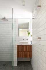 The bathroom on the second level is outfitted with terrazzo tile flooring, ceramic mosaic tile on the walls, and a walnut vanity.