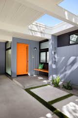 A built-in bench painted a bright orange to match the front door offers warmth, convenience, and a playful vibe for the entrance.
