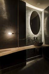 The guest bathroom features an organically shaped wooden table, which is suspended on copper and rests against the textured stucco wall.


