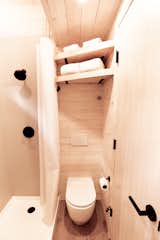 The compact bathroom is surprisingly large with a vanity, wall-hung toilet, and a spacious walk-in shower with a window. 