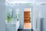 Simple, white tile extends from floor-to-ceiling in the bathroom. A clerestory window draws in daylight, further reflecting off the glossy surfaces to create a light-filled interior space.