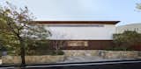 The home is concealed behind horizontal bands of materials including Aji stone quarried from Shikoku, a powder-coated aluminum screen (lath), the white plaster exterior of the second floor, and a titanium zinc alloy roof.