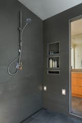 The wet room connects to two half-baths on either side that are equipped with dual-flush toilets and WaterSense fixtures. Gray porcelain tiles from Statements Tiles line the room.
