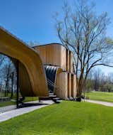 The undulating wood-and-steel structure is engineered to hide a 90-foot steel structural beam that supports the cantilevered canopy and creates the illusion of a floating pavilion from the front.
