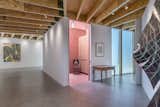 The small, salmon-pink powder room offers a pop of color in the otherwise neutral gallery/corridor space. The painting in the background is by Steve Rodin, and the print above the table is by Jim Isermann.