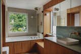 The timber joinery in the bathroom conceals storage that allows the family home to remain uncluttered. The large windows frame green views that belie the urban context and complement the refined material palette.