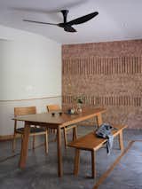 The brick wall of the dining area in this Singapore home is new from the remodel by Goy Architects. Its presence celebrates the building's heritage and brings warmth into the space, like a hearth. The wood table matches the hues in the timber floor elements and plays well with the accent wall, pulling the room's simple and earthy aesthetic together. The addition of the accordion doors opens the dining room out to the patio, giving the users the best of indoor and outdoor dining.