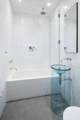 A second bathroom maintains the open brightness of the rest of the loft with simple white tiling and a transparent pedestal sink.
