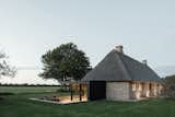 This thatch-roofed brick cottage in Nieby, Germany, was originally built by tenant farmers or crofters from a nearby estate in the late 1800s. It stands on a small triangular plot of land surrounded by barley fields and faces toward the Geltinger Birk nature reserve. The home’s street-facing facade was preserved and restored with only a minimal, black-steel dormer window belying the more substantial alterations which open onto the private rear yard. A subtle black-framed addition containing an oak-lined living space is tucked under the thatched roof and opens onto a sunken timber terrace while large picture windows are cut into the historic brick volume in areas which had been damaged from the previous additions.